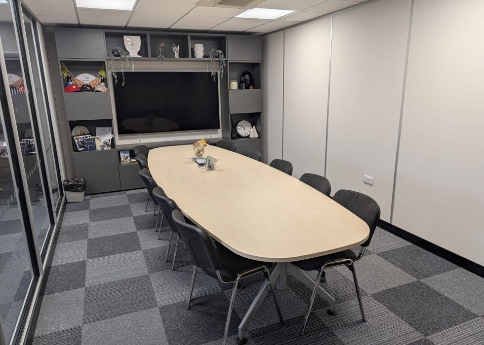 Conference room with an oval table, chairs, a wall-mounted TV, and a collage of company history photos labelled 'Hampsons History
