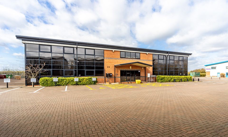Exterior of a modern brick office building with large glass windows and an empty car park in front.