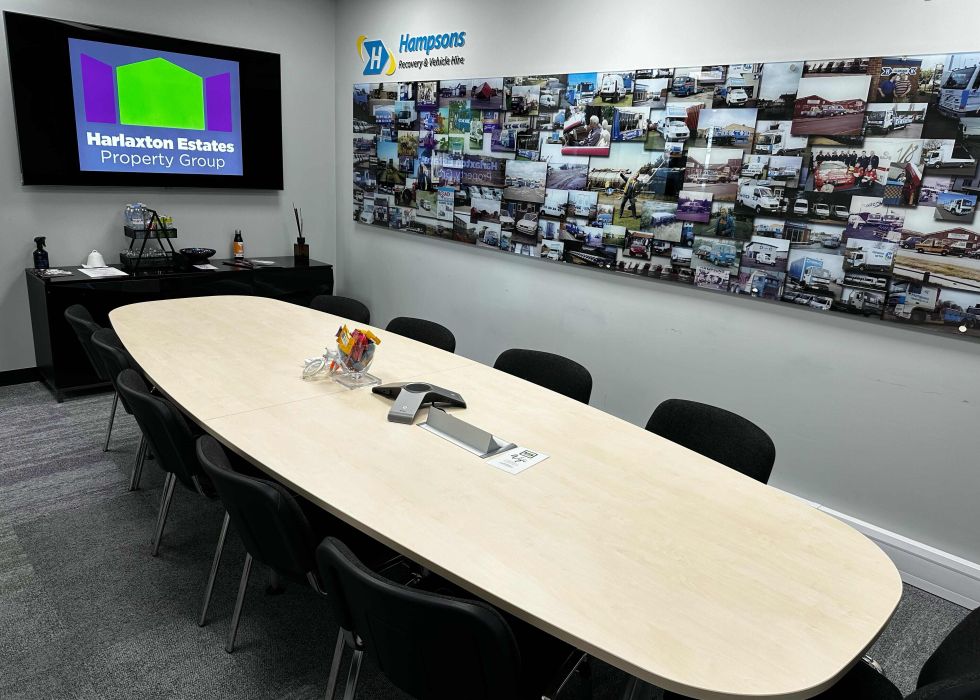 Conference room with an oval table, chairs, a wall-mounted TV, and a collage of company history photos labelled 'Hampsons History